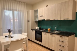 A modern kitchen with light wood cabinets, a black countertop, and a green backsplash. There is a dining table with chairs and a vase with flowers.