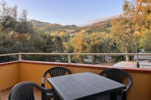 Ein Balkon mit Tisch und Stühlen, der auf eine hügelige Landschaft mit Bäumen und Gebäuden blickt.