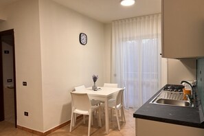 Una cocina compacta con zona de comedor, un reloj en la pared y una ventana con cortinas.