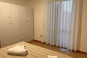 Ein Hotelzimmer mit einem Bett, einem großen Kleiderschrank und einem Fenster mit durchsichtigen Vorhängen.
