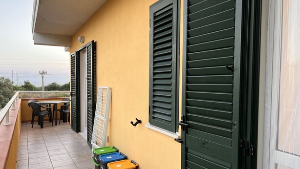 Ein Balkon mit Tisch und Stühlen, grüne Fensterläden und Mülltonnen.