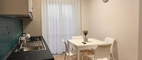 A compact kitchen with a gas stove, sink, and white chairs around a small table.