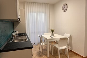 Eine kleine Küche mit Gasherd, Spüle und weißen Stühlen um einen kleinen Tisch.