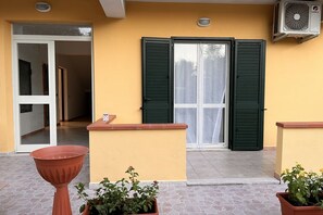A building entrance with a sliding glass door, a small outdoor seating area with a terracotta planter, and a potted plant.