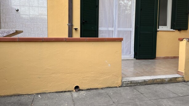 Ein Gebäude mit gelber Fassade, einer gefliesten Eingangszone und grünen Fensterläden.
