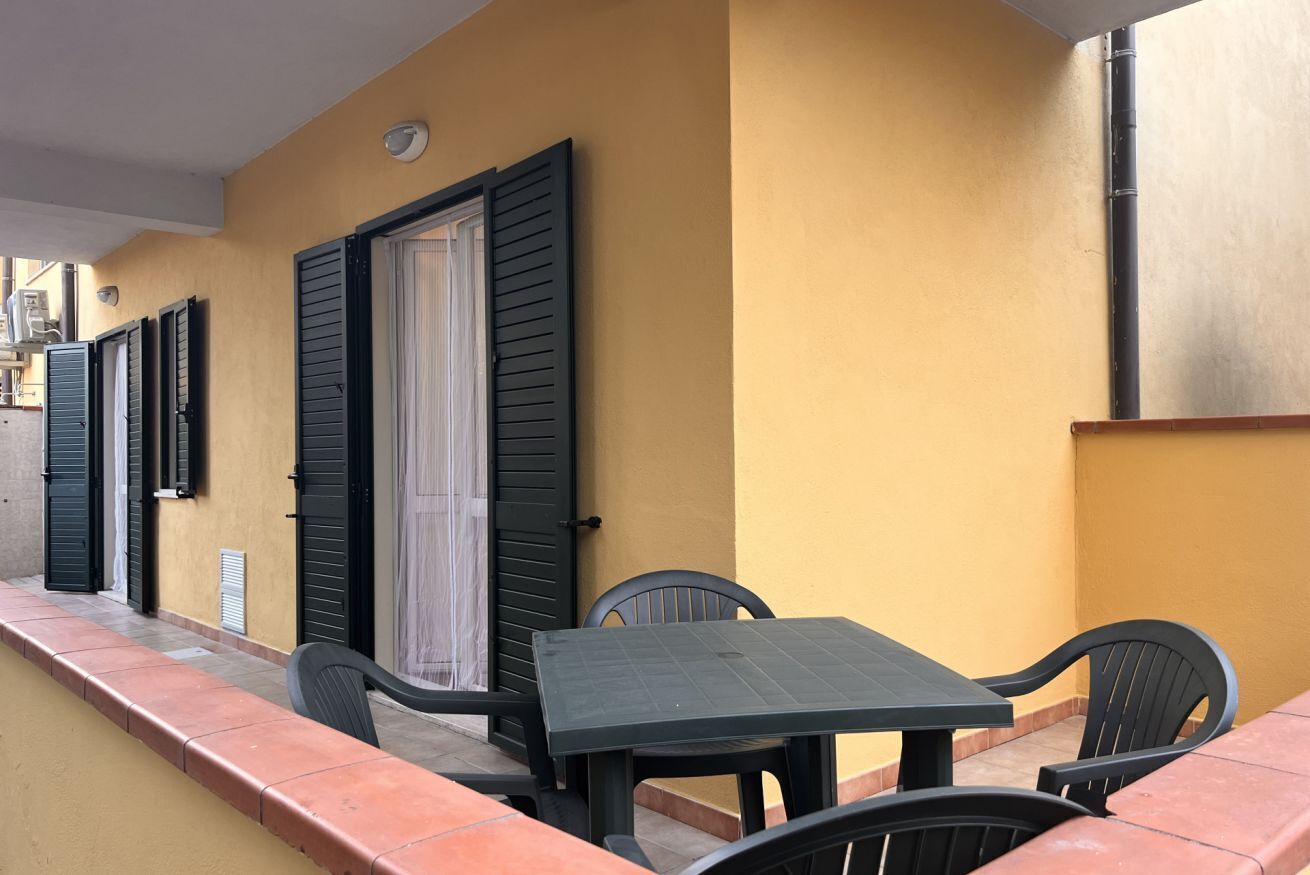 Un pequeño patio al aire libre con una mesa y sillas, una puerta con contraventanas y una pared amarilla.