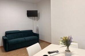 Ein Zimmer mit einem türkisfarbenen Sofa, einem weißen Tisch mit Blumen und einem an der Wand befestigten Fernseher.