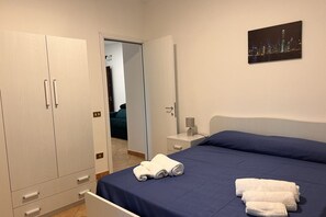 A hotel room with a bed, a wardrobe, a nightstand, and a cityscape painting.