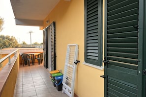 Een balkon met betegelde vloer, een tafel met stoelen en een raam met groene luiken.