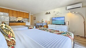 Hotellihuone, jossa on sänky, televisio, pieni keittiö ja merinäköala.