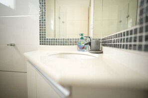 Un bagno con un lavandino bianco, un rubinetto e una bottiglia di sapone per le mani.