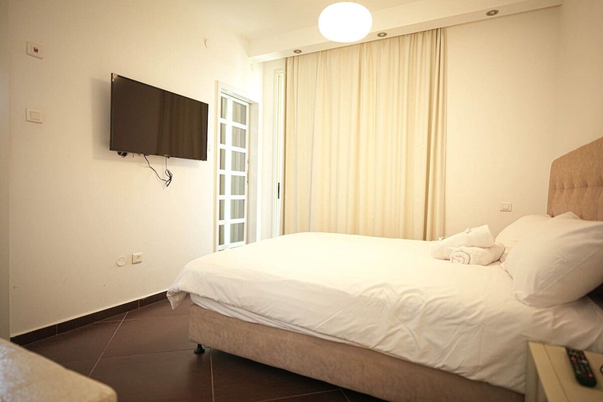 Une chambre d’hôtel avec un lit, un téléviseur fixé au mur, une fenêtre avec des rideaux et une table de chevet avec une télécommande.