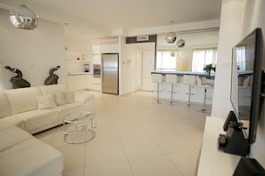 A modern kitchen with a refrigerator, a dining area with bar stools, and a living room with a sofa and coffee table.