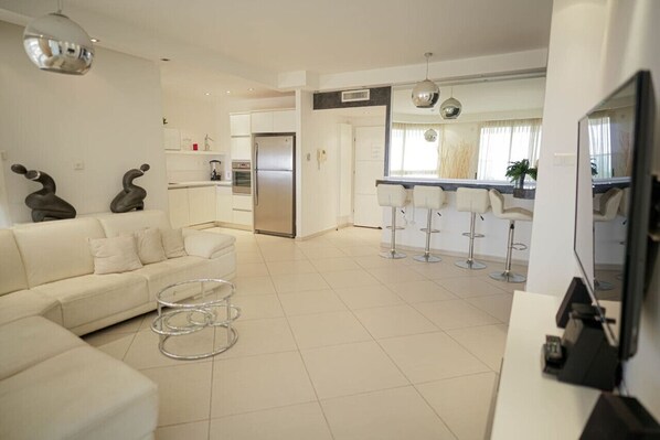 A modern kitchen with a refrigerator, a dining area with bar stools, and a living room with a sofa and coffee table.