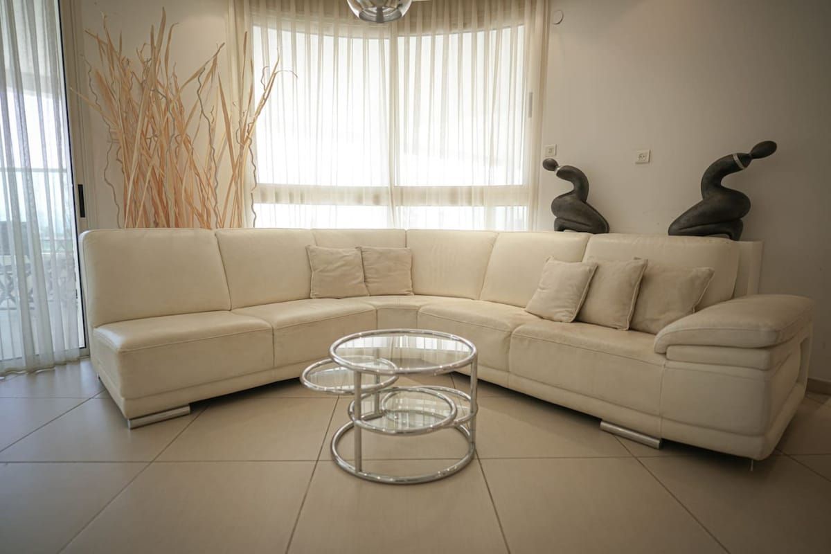 Una sala de estar moderna con un sofá seccional color beige, una mesa de centro de vidrio y esculturas decorativas en la pared.