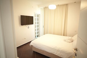A bedroom with a bed, a television mounted on the wall, a door, and a window with curtains.