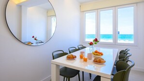 Un coin repas avec une table blanche, des chaises vertes et un miroir rond accroché au mur.