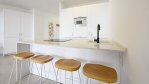 Une cuisine moderne avec des meubles blancs, un îlot central doté de tabourets et un four à micro-ondes encastré.