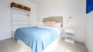 Une chambre à coucher avec un lit, deux tables de chevet blanches, une armoire blanche et une couverture bleue.