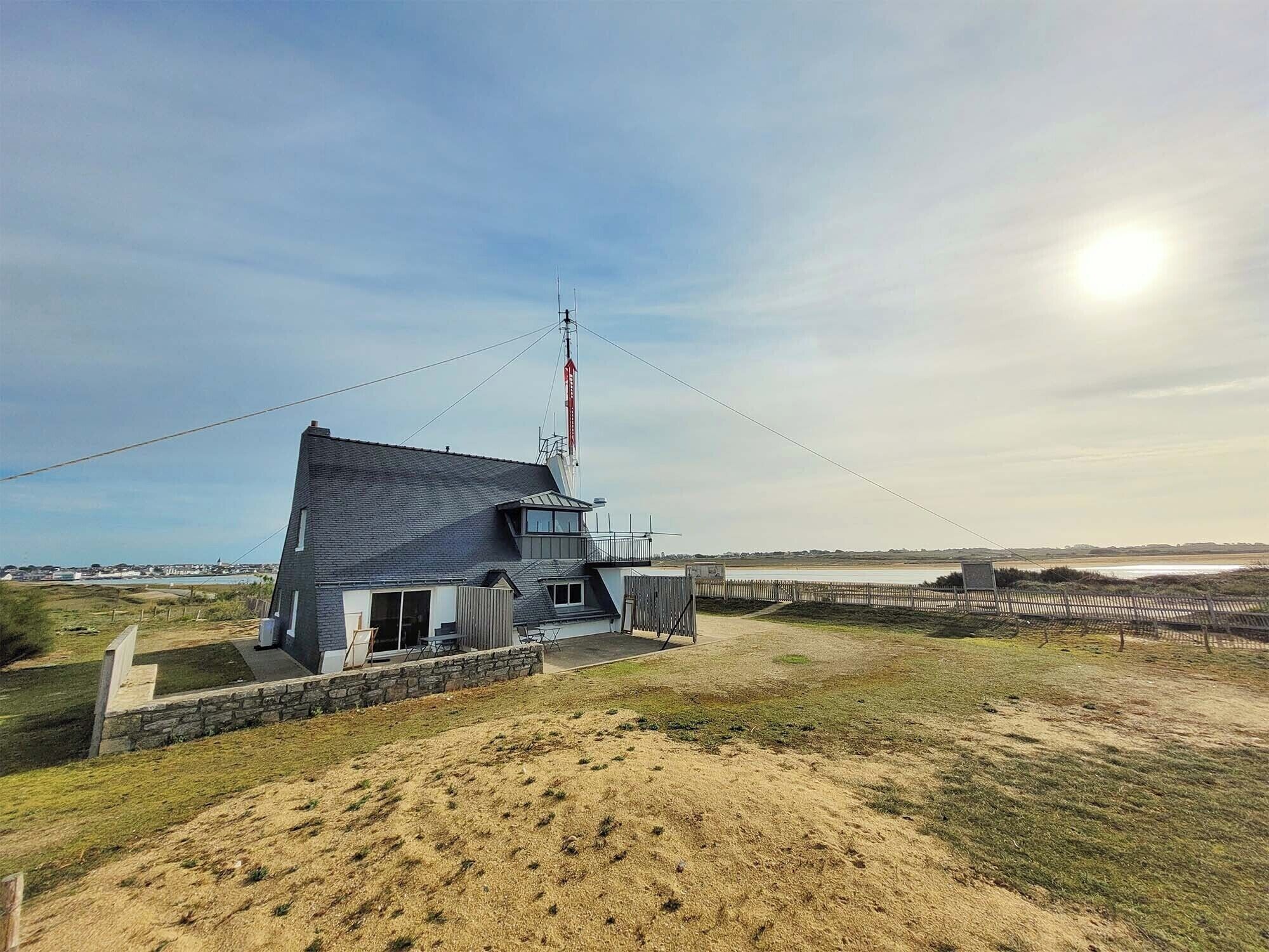Una casa moderna con una antena grande, ubicada en una colina cubierta de hierba y vistas al mar.