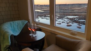 A room with a view of a frozen landscape through a window, a table with two glasses of wine, and a blue towel on a chair. - Ocean Oasis - Beachfront Condo with breathtaking views (Hampton)