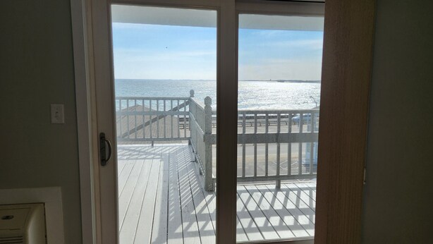 A view from a room with a sliding glass door to a wooden deck overlooking a body of water. - Ocean Oasis - Beachfront Condo with breathtaking views (Hampton)