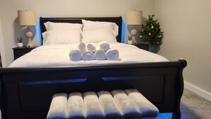 A neatly made bed with white linens and rolled towels, a dark wooden headboard, and a small bench with towels. - Ocean Oasis - Beachfront Condo with breathtaking views (Hampton)
