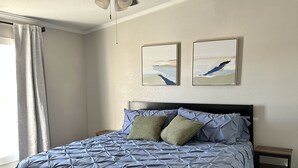 A bedroom with a bed, a ceiling fan, two wall-mounted paintings, a nightstand, and a window with curtains. - SEVEN National Parks w/in 2 hrs. Come EXPLORE. Come PLAY. Come RELAX...REPEAT!!! (Kanab)