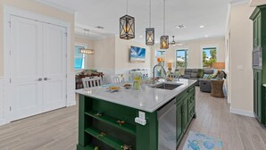 A modern kitchen with a central island, green cabinetry, pendant lighting, and a view to the living area. - Lucky Turtle, newly built Private House with Swimming Pool (South Padre Island)