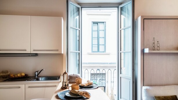 Eine kompakte Küche mit Essbereich, Blick auf einen Balkon und einem Bett mit Kopfteil.
