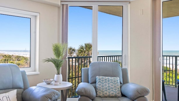 A balcony with two leather armchairs, a small table with a bowl and plates, and a potted plant.