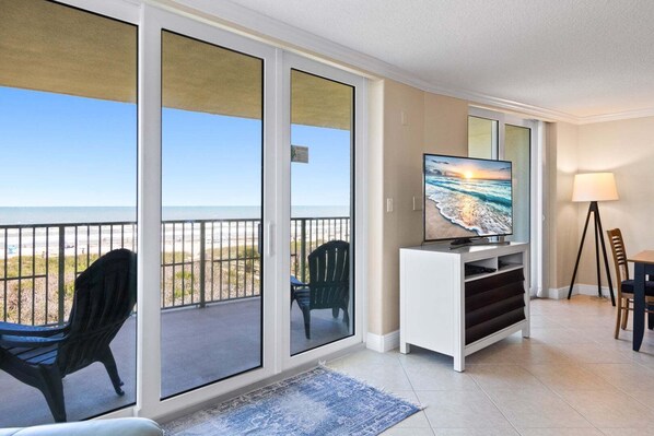 A balcony with a view of the beach, a television on a stand, and a lamp.