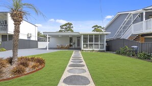 Une maison moderne dotée d’un patio couvert, d’une pelouse avec un chemin en pierre et d’une cour arrière clôturée.