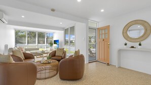 Un salon spacieux doté d’une grande fenêtre, d’un miroir rond et d’une porte donnant sur l’extérieur.