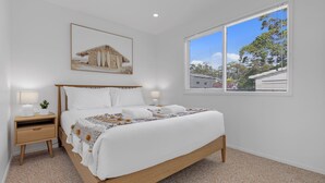 Une chambre à coucher comprenant un lit, deux tables de chevet, une fenêtre avec des stores et un tableau accroché au mur.