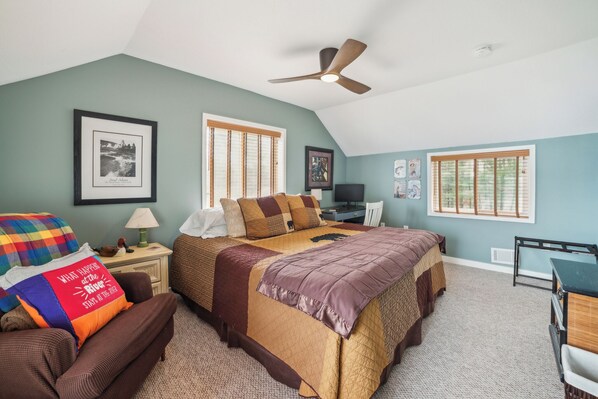 A bedroom with a large bed, two windows, a ceiling fan, and a desk.