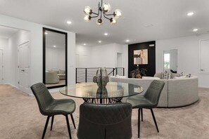 Una sala de estar moderna con una mesa de centro de vidrio, sillones de cuero, una mesa de comedor redonda y una lámpara de araña original.