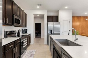A modern kitchen with dark cabinets, stainless steel appliances, and a marble backsplash.
