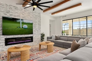 Una sala de estar moderna con televisor de pantalla plana, chimenea, sofá gris y ventanas amplias.