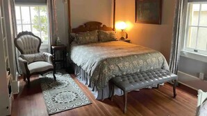 Un dormitorio con una cama grande, una silla, un banco, una mesita de noche y una lámpara.