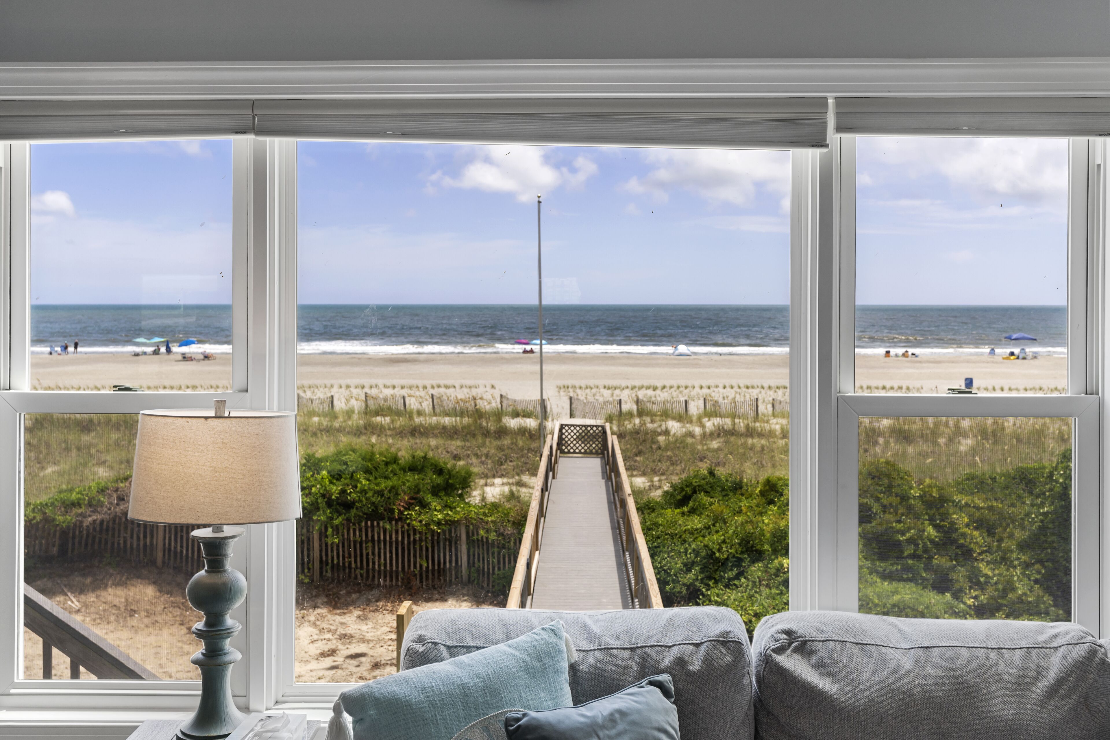A room with a view of the beach, a lamp, and a sofa with cushions.