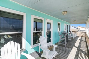Une véranda couverte avec des fauteuils Adirondack blancs, une terrasse en bois et une vue sur l’océan.
