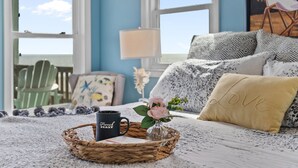 A cozy bedroom with a bed, a wicker tray with a mug, a vase with flowers, and a chair by the window. - "Narwhal Nest" Newly remodeled, 5 bed/3 bath, oceanfront home! (Supply)