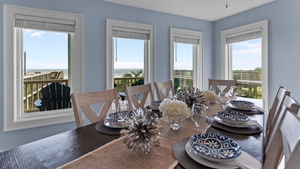 A dining area with a view of the ocean, a ceiling fan, and a table set with blue and white plates and white flowers. - "Narwhal Nest" Newly remodeled, 5 bed/3 bath, oceanfront home! (Supply)