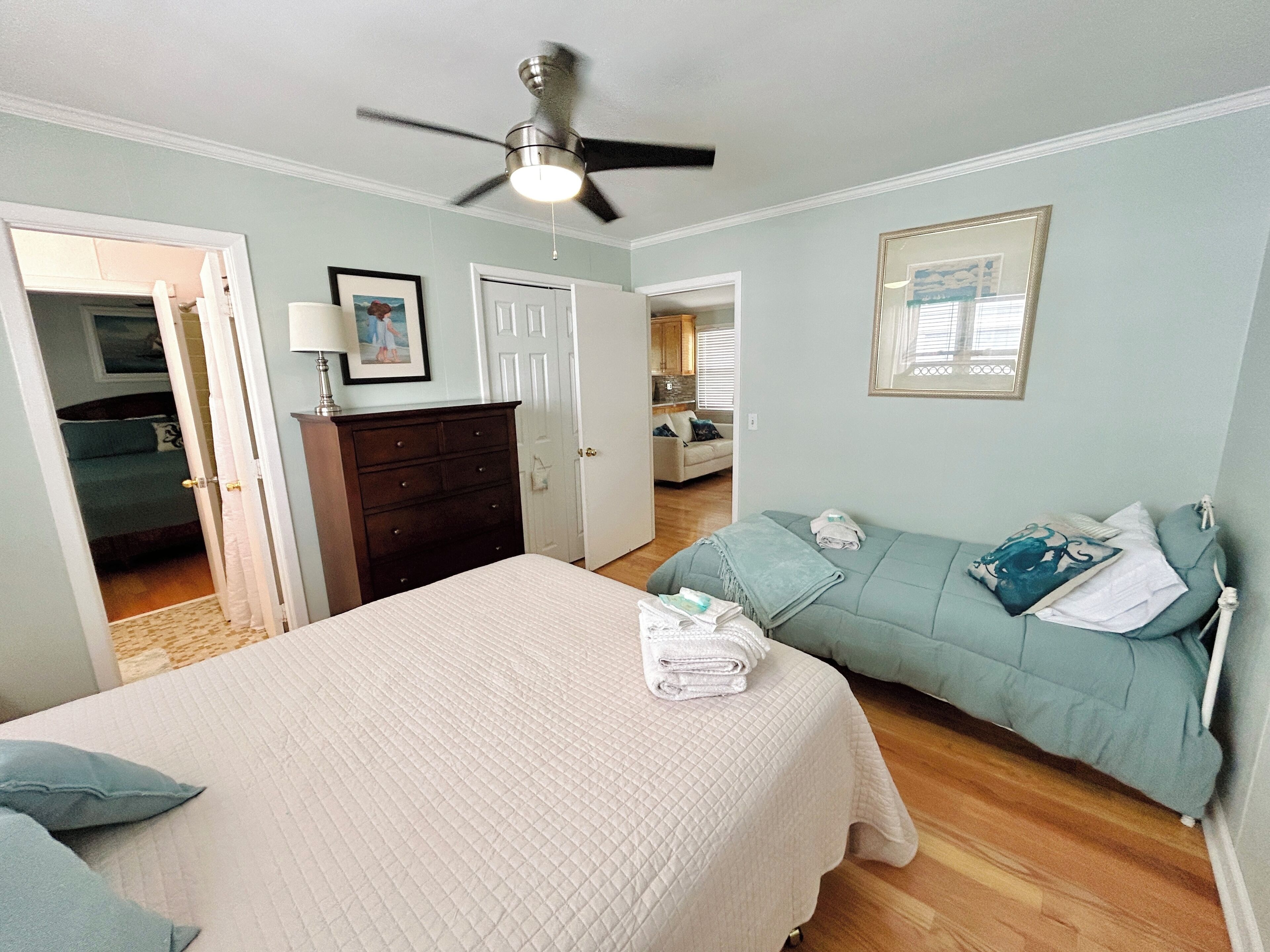 A bedroom with a bed, a dresser, a ceiling fan, and a view into the kitchen.