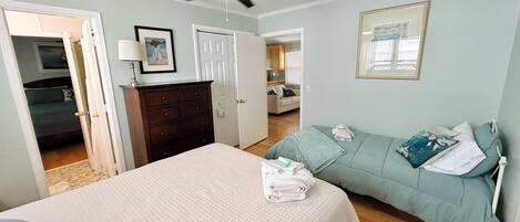 A bedroom with a bed, a dresser, a ceiling fan, and a view into the kitchen.