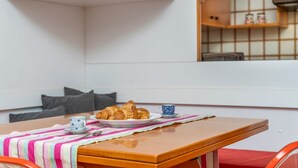 A corner dining area with a table, a television above, and a kitchen area in the background.
