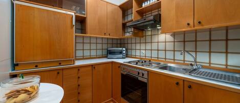 Een koelkast, een oven, een kookplaat, kookgerei, borden en bestek