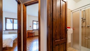 A bedroom with a wooden door, a bathroom with a glass shower, and a view of a dining area.