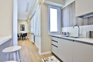 A modern kitchen with a window, a dining area, and a small bar stool. - GuestHost - Maison La Fontana Apartment (Napoli)